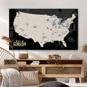 May include: A large wall art piece depicting a map of the United States in black and white. The map highlights stadium locations with small black circles. Text at the bottom reads "PRO SPORTS STADIUM TOUR". A quote is on the right side.