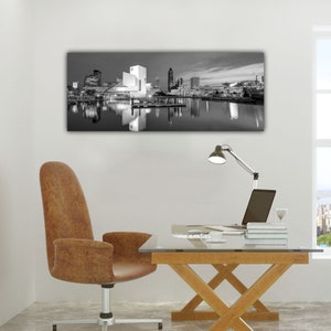 Puede incluir: Fotograf&iacute;a en blanco y negro de un horizonte urbano reflejado en una masa de agua. El horizonte presenta edificios altos, incluido un edificio moderno con un dise&ntilde;o &uacute;nico. La fotograf&iacute;a est&aacute; enmarcada y colgada en una pared blanca.