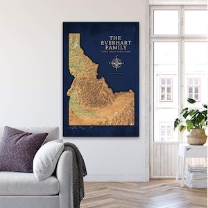 May include: A blue and gold map of Idaho with the text "The Everhart Family Home Sweet Home State" and a compass rose. The map is framed and hanging on a white wall.