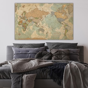 May include: A vintage-style world map with a light blue background and brown continents. The map is framed and hanging above a gray bed with pillows and blankets.