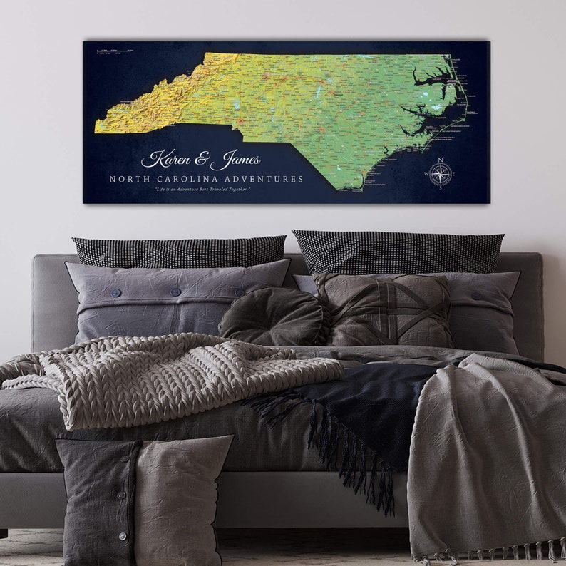 Puede incluir: Un mapa personalizado de Carolina del Norte con un fondo azul y un mapa en degradado amarillo y verde del estado. El mapa se titula "Karen & James North Carolina Adventures" con el lema "La vida es una aventura que se vive mejor juntos".