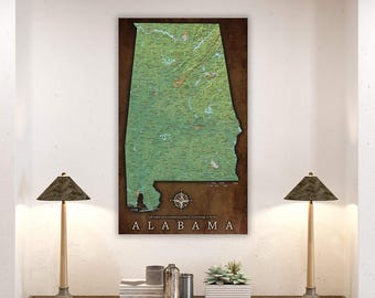 May include: A vintage-style map of Alabama with a green and brown color scheme. The map is framed and hanging on a white wall. The text "Life takes us to unexpected places. Love brings us home." and "ALABAMA" are printed below the map.