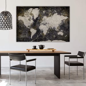 May include: A black and white world map print with a distressed, vintage look. The map is framed and hanging on a white wall above a wooden table with two black chairs.
