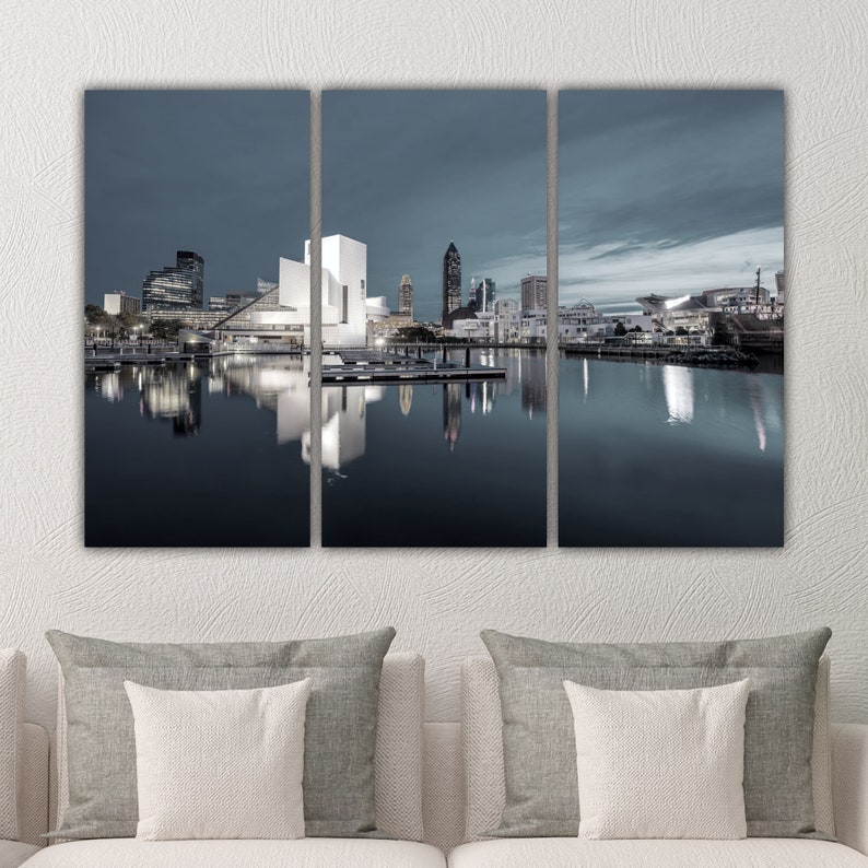 Puede incluir: Una vista panor&aacute;mica de un horizonte urbano al atardecer, con un gran edificio blanco en primer plano y un rascacielos alto en el fondo. La ciudad se refleja en las aguas tranquilas de un lago o r&iacute;o.