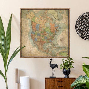 May include: A framed vintage-style map of North America, featuring a detailed depiction of countries and states in various colors. The map includes text that reads "Better to See Something Once Than to Hear About It a Thousand Times." The map is displayed on a light-colored wall.