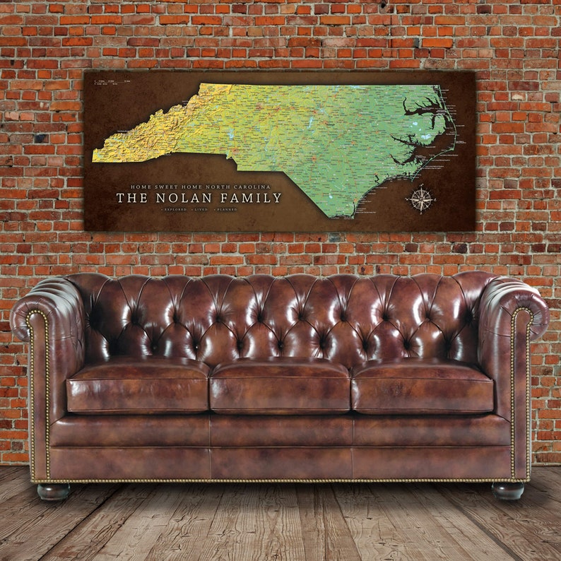 Puede incluir: Un sof&aacute; de cuero marr&oacute;n con capiton&eacute; de botones se encuentra frente a una pared de ladrillo con un mapa personalizado de Carolina del Norte colgado encima. El mapa est&aacute; titulado "Home Sweet Home North Carolina, The Nolan Family".