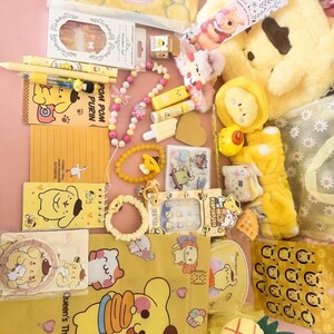 May include: A collection of yellow and pink themed merchandise, including a plush pencil case, notebooks, pens, lip balms, bracelets, and a plush Winnie the Pooh bag. The items feature cartoon characters and the text "Queen's Theme."