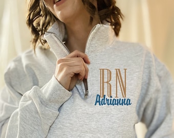 May include: A gray sweatshirt with a zipper and a brown embroidered design that says "RN Adrianne".