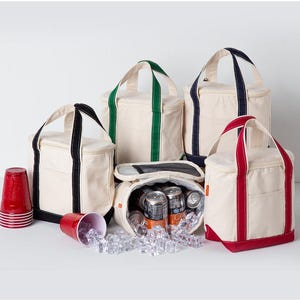 Peut inclure: Quatre sacs isothermes en toile cr&egrave;me avec des bordures noires, vertes, bleu marine et rouges. Chaque sac poss&egrave;de deux anses et une poche avant. Un sac est ouvert, r&eacute;v&eacute;lant une doublure en aluminium, des canettes et des gla&ccedil;ons. Deux gobelets rouges.