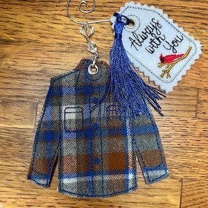 Puede incluir: Un adorno de tela con forma de camisa a cuadros en azul, marr&oacute;n y gris, con un colgador de metal plateado y cuentas transparentes. Incluye una etiqueta blanca festoneada con el texto Always with You y un cardenal rojo, adem&aacute;s de una borla azul.