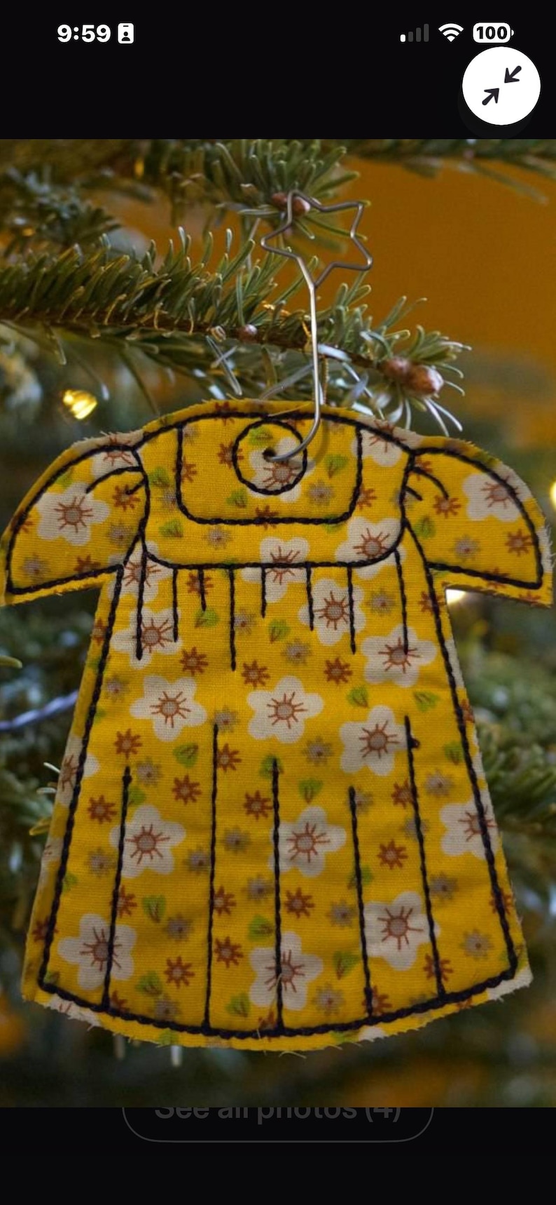 Puede incluir: Un adorno de tela amarillo con forma de vestido y estampado floral blanco y marr&oacute;n. El adorno presenta contornos y l&iacute;neas verticales cosidas en negro, con un gancho de metal plateado en forma de estrella fijado en la parte superior.