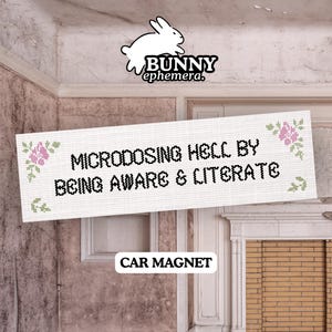 Op de afbeelding: Een rechthoekige automagneet met een wit kruissteekpatroon, roze bloemaccenten en de zwarte tekst "MICRODOSING HELL BY BEING AWARE & LITERATE". Boven de magneet staat een wit konijnenlogo met de tekst "BUNNY ephemera."