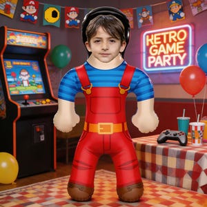 Peut inclure: Un costume gonflable d'un personnage en salopette rouge, chemise rayée bleue et casque noir. Le costume est devant une borne d'arcade rétro et une enseigne "Retro Game Party". Ballons et fournitures de fête en arrière-plan.