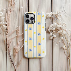 May include: A white iPhone case with a pattern of yellow vertical stripes and blue vertical stripes. The case has a repeating pattern of blue flowers and yellow lemon slices. The case has a camera cutout.