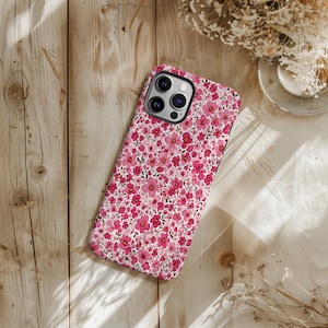Puede incluir: Funda de tel&eacute;fono con dise&ntilde;o floral. La funda est&aacute; cubierta con un patr&oacute;n de peque&ntilde;as flores rosas sobre un fondo blanco. Tiene un borde negro y un recorte para la c&aacute;mara. El dise&ntilde;o es un patr&oacute;n repetitivo de flores rosas y hojas verdes.