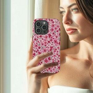 Puede incluir: Funda de tel&eacute;fono con un dise&ntilde;o floral rosa. El dise&ntilde;o presenta peque&ntilde;as flores rosas sobre un fondo blanco. La funda tiene un m&oacute;dulo de c&aacute;mara negro y se sostiene en una mano.