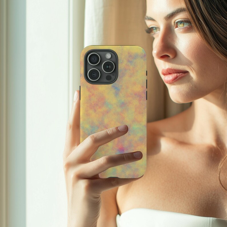 May include: A smartphone case with a colorful abstract design in shades of yellow, pink, and blue. The case has a smooth finish and a camera cutout. The phone case is held in a person's hand.