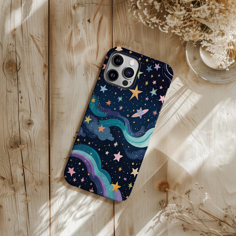May include: A smartphone case with a whimsical night sky design. The case features a dark blue background with colorful stars, a rainbow, and flowing, cloud-like shapes. The case is made of a durable material and has a protective design.