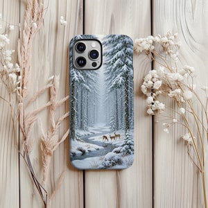 May include: A phone case featuring a winter forest scene with snow-covered trees, a stream, and deer. The case has a glossy finish and a camera cutout.