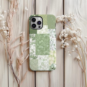 Peut inclure: Coque de téléphone à motifs floraux verts et blancs. L'étui présente un motif patchwork avec divers motifs botaniques dans des tons de vert et de blanc. La coque est présentée sur une surface en bois clair avec des fleurs séchées.