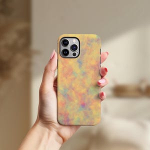 May include: A yellow phone case with a colorful, abstract design. The case features a pattern of blended colors including yellow, orange, pink, blue, and purple. The phone case has a camera cutout and a black border.