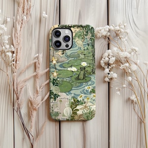 May include: A phone case with a tranquil pond design, showing a frog on a lily pad, with water lilies and daisies. The case has a green and beige colour scheme, with the word "healing" visible.