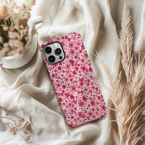 Puede incluir: Una funda de tel&eacute;fono con un dise&ntilde;o floral. La funda presenta un dise&ntilde;o repetido de peque&ntilde;as flores rosas sobre un fondo blanco. La funda del tel&eacute;fono se muestra sobre una tela blanca.