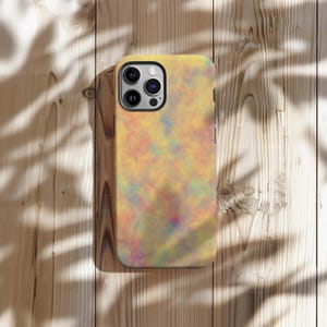 May include: A yellow phone case with a colorful, abstract design. The case features a pattern of blended colors including yellow, orange, pink, blue, and green. The phone case is shown on a wooden surface with shadows.