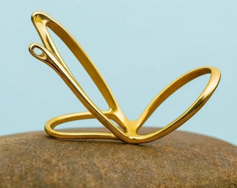 May include: A gold-colored, abstract sculpture resembling a needle and thread. The sculpture is placed on a brown stone, with a light blue background. The needle's eye is clearly visible, and the thread appears to loop around the sculpture.