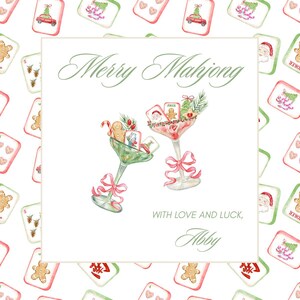 May include: A watercolour illustration featuring the text "Merry Mahjong" and two martini glasses filled with Christmas-themed mahjong tiles and decorations. The glasses are tied with pink bows. The background has repeating Christmas mahjong tiles.