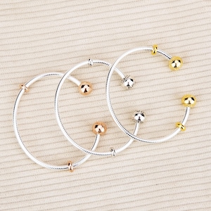 Könnte beinhalten: Drei silberne Armbänder mit dekorativen goldenen, roségoldenen und silbernen Perlen. Die Armbänder haben ein schlichtes, elegantes Design, perfekt für den Alltag. Die Perlen verleihen den Armbändern einen Hauch von Raffinesse.