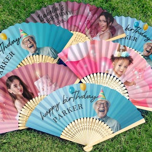 May include: A selection of personalised paper fans with bamboo handles, each displaying a photograph and birthday message. The fans feature images of people and the text "happy birthday" and names. The background colours are pink and blue.