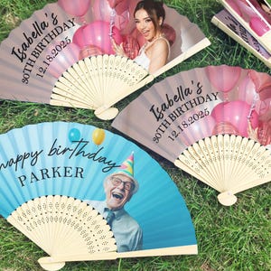 May include: A collection of personalised paper fans. Two fans display a woman with pink balloons and the text "Isabella's 30th Birthday 12.18.2025." Another fan has a blue background with the text "Happy Birthday Parker" and a photo of a man.
