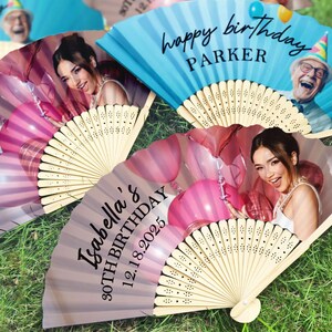 May include: A collection of open hand fans, each featuring a birthday message and a photograph. One fan is blue with "happy birthday PARKER" printed on it. Other fans are pink and grey with a photo of a woman and the text "Isabella's 30TH BIRTHDAY 12.18.2025".