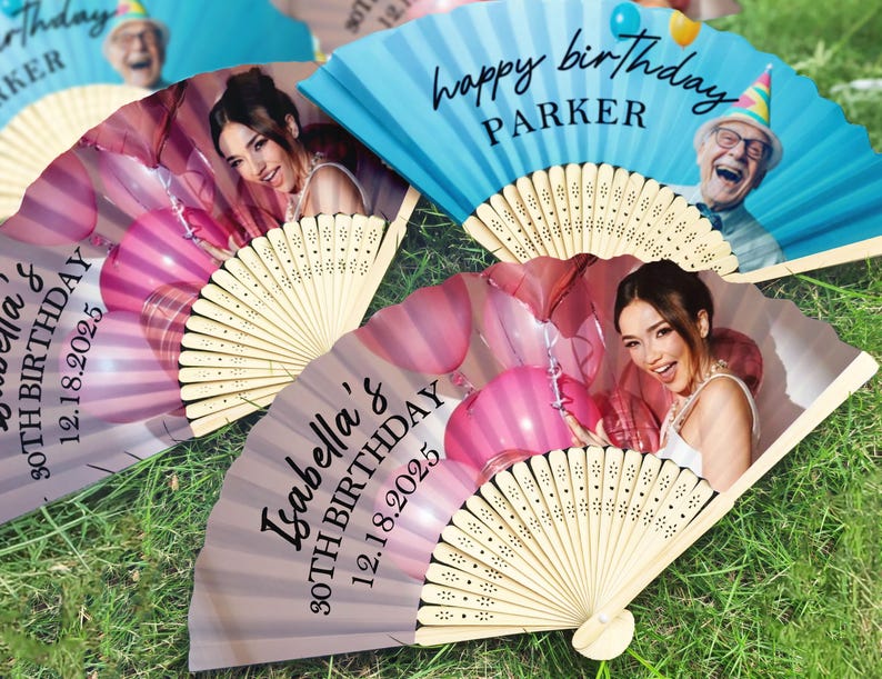 May include: A collection of open hand fans, each featuring a birthday message and a photograph. One fan is blue with "happy birthday PARKER" printed on it. Other fans are pink and grey with a photo of a woman and the text "Isabella's 30TH BIRTHDAY 12.18.2025".