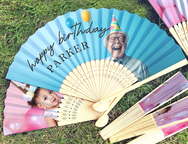 May include: A selection of personalised birthday fans. One fan displays a photo of a laughing senior with a party hat, the text "happy birthday PARKER", and balloons. Another fan shows a baby. Other fans have pink and purple stripes.