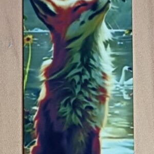 May include: Bookmark featuring a fox with orange and white fur, gazing at a butterfly. The bookmark has a hole at the top and depicts a serene scene with water, flowers, and a butterfly.