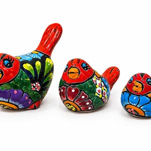 May include: Three ceramic bird figurines of varying sizes, each featuring a vibrant hand-painted floral pattern in red, blue, green, purple, and yellow. The birds have rounded bodies, prominent red heads, and stylized black outlines on their wings.