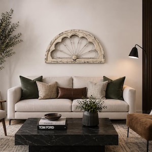May include: A living room set featuring a beige sofa with green and brown throw pillows, a black marble coffee table, a brown armchair, and a light-colored armchair. A semi-circular white distressed wooden wall decor hangs above the sofa.