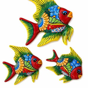 May include: Three decorative fish wall ornaments featuring vibrant hand-painted patterns in red, yellow, blue, and green. Each fish displays a glossy finish with intricate floral and geometric details on the body, fins, and tail, showcasing a colorful design.