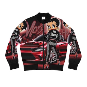 Può includere: Un giubbotto bomber nero con una stampa all-over di un personaggio dei cartoni animati con capelli neri che indossa una giacca con la scritta Mz Boop, in piedi davanti a un'auto sportiva rossa. Il design include testo rosso neon e bordi a coste.