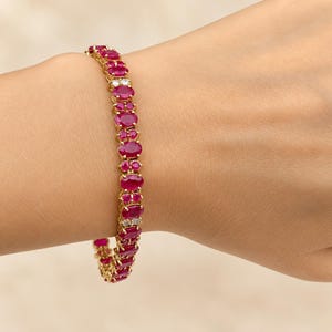May include: A gold link bracelet featuring a series of oval-cut deep red rubies alternating with small, clear round-cut diamonds. The stones are set in a yellow gold metal frame, creating a continuous line of vibrant red and sparkling white accents.
