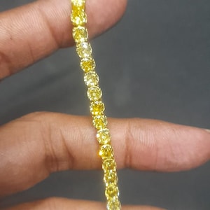 May include: A tennis bracelet featuring a continuous row of round, vibrant yellow stones set in a metallic frame. The stones are uniform in size and shape, creating a bright, reflective line of yellow color that spans the length of the bracelet.