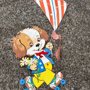 May include: A paper cutout of a dog wearing roller skates and holding a bouquet of yellow flowers. The dog is wearing a blue jacket, yellow pants, and a red bow tie. The dog is holding a red, white, and blue striped kite.