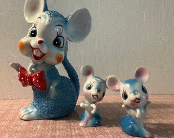 May include: Three blue ceramic mouse figurines. The largest mouse is wearing a red bow with white polka dots. All three mice have white ears and black eyes.