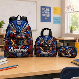 May include: A blue, red, and silver backpack, lunch bag, and pencil case set featuring a graphic of the character Optimus Prime and the name Andew printed in white. Each item displays the Autobot logo and a dynamic, fiery background design.