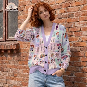 May include: A long-sleeved V-neck cardigan featuring a repeating patchwork pattern of colorful cartoon characters and floral motifs in shades of purple, pink, and blue, finished with a solid light purple button-down placket and ribbed cuffs.