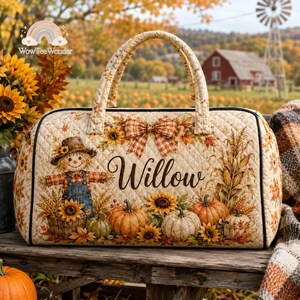 May include: A quilted duffel bag featuring a fall-themed print with a scarecrow, pumpkins, sunflowers, and corn stalks. The name Willow is printed in black script in the center, accented by a plaid bow. The bag has two handles and black trim.