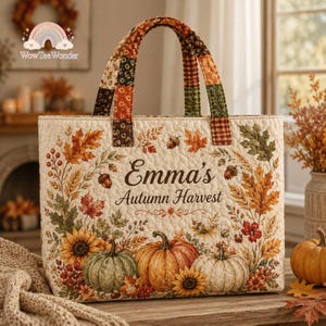 May include: A quilted tote bag featuring a cream background with a colorful autumn harvest print of pumpkins, sunflowers, and fall leaves. The text "Emma's Autumn Harvest" is printed in the center. It has two fabric handles with a patchwork pattern.