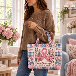 Op de afbeelding: Een gewatteerde tas met een patchworkontwerp van blauw-witte vichyruitjes en roze bloemenpatronen. Het middenpaneel toont een roze bewustzijnslint omringd door bloemillustraties en de tekst Hope Grows Here, Believe, Brave.